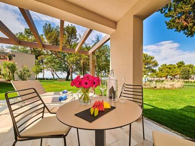 Terrasse avec table et chaises donnant sur un jardin et un ciel bleu par une journée ensoleillée.