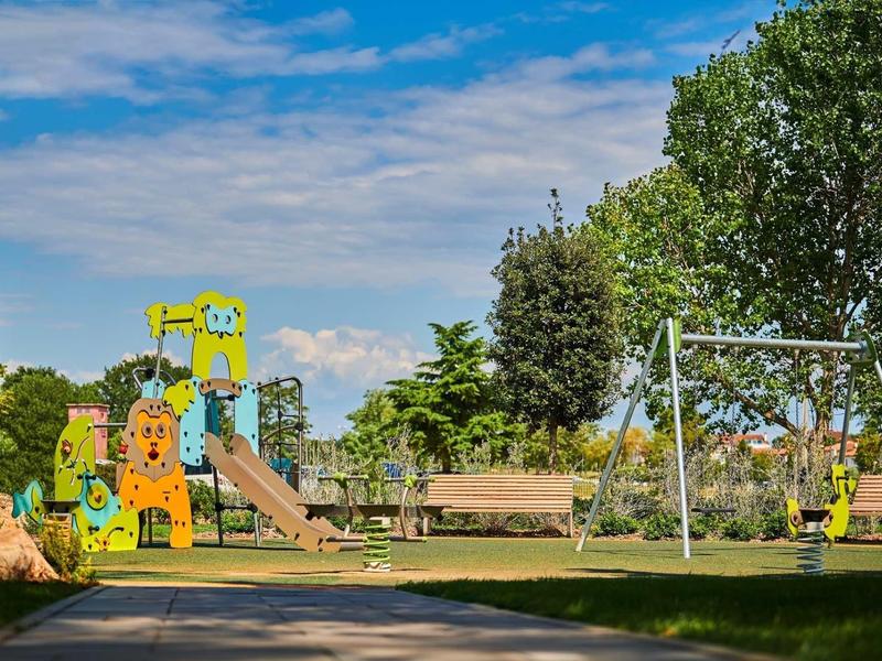 Parco giochi colorato per bambini con scivolo, struttura per arrampicarsi e altalene in un parco soleggiato.
