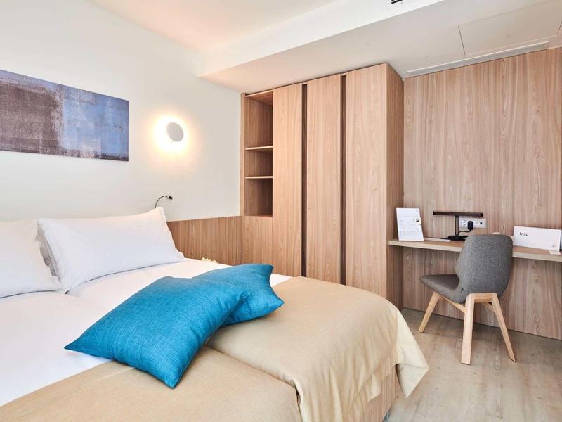 Camera d'hotel moderna con letto, cuscini blu, mobili in legno e scrivania con sedia.