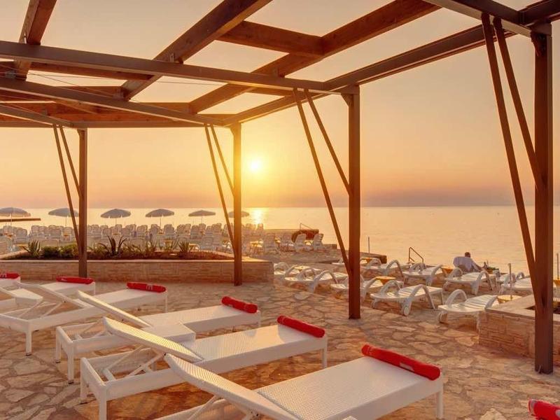 Tramonto su una spiaggia con lettini e pergolati in legno.