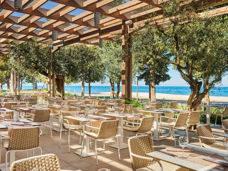 Ristorante all'aperto con pergolato in legno, molti tavoli e vista sul mare.