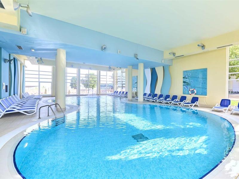 Piscina interna luminosa con sedie a sdraio blu e grandi finestre