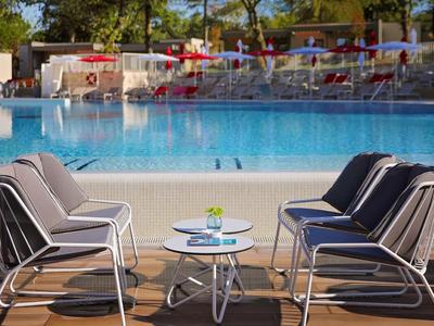 Poolbereich mit modernem Sitzbereich und blauem Wasser unter Bäumen.