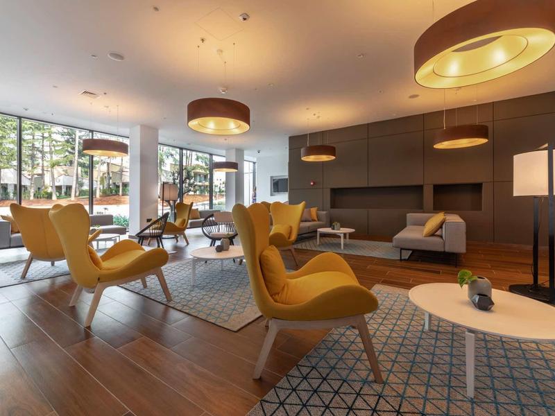 Area lounge moderna dell'hotel con poltrone gialle, pavimento in legno e grandi finestre.