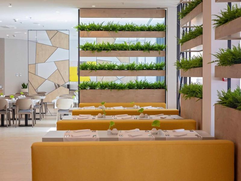 Ristorante moderno con panche gialle e piante verdi su mensole a parete.