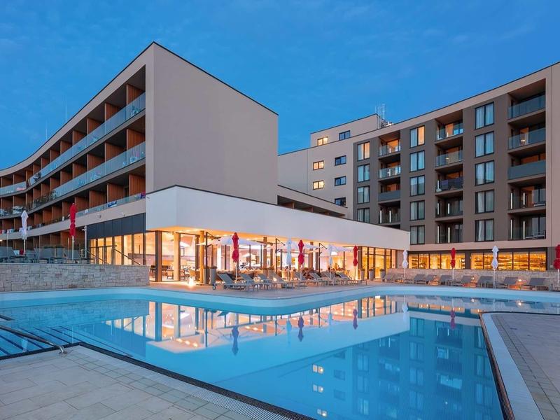 Hotel moderno con piscina illuminata e grandi finestre di vetro al crepuscolo.