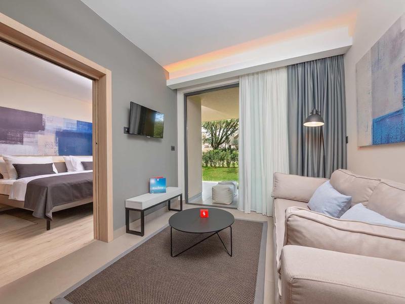 Camera d'hotel moderna con divano, TV e vista sul giardino.