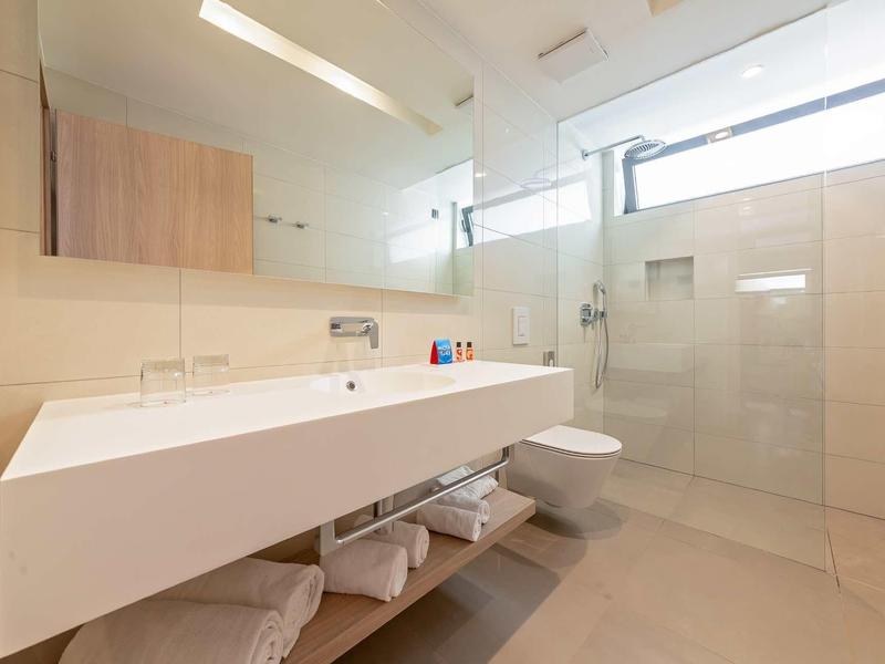 Bagno moderno con grande specchio, lavabo e doccia a filo pavimento.