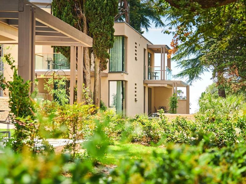 Edificio di un hotel moderno circondato da rigogliosa vegetazione e alberi in una giornata di sole.