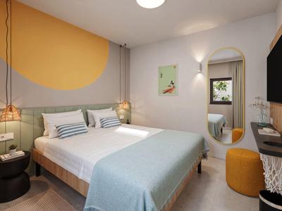 Chambre d'hôtel moderne avec lit double, miroir mural et télévision aux couleurs chaudes.