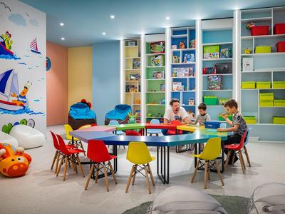 Des enfants sont assis à une table colorée dans une salle de classe bien équipée avec des étagères et des décorations murales.