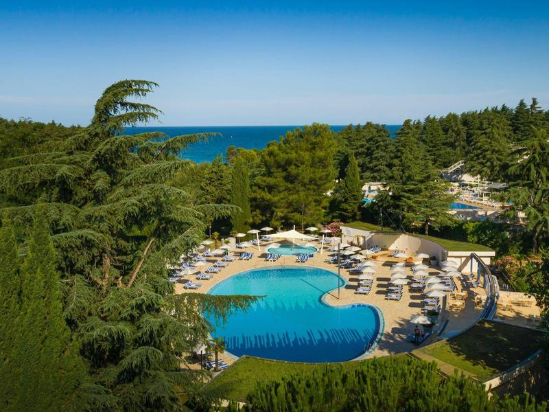 Piscine extérieure ronde avec transats entourée d'arbres et vue sur la mer