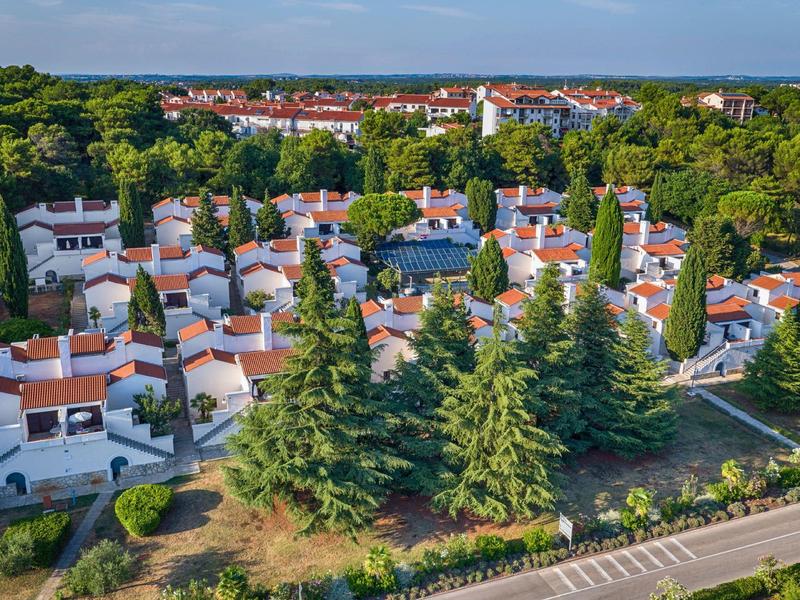 Vue aérienne d'un village de vacances avec de petites maisons blanches aux toits rouges, entourées d'arbres.