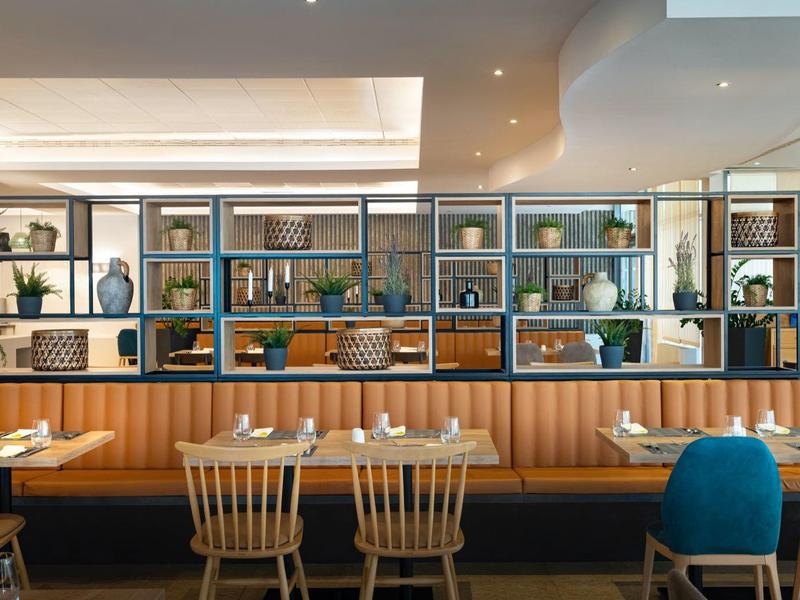 Restaurant moderne avec tables en bois, chaises et étagères décoratives le long du mur.