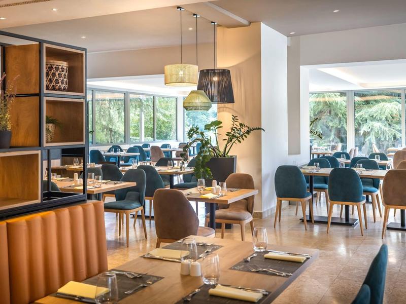 Restaurant moderne avec tables, chaises et grandes fenêtres donnant sur un jardin