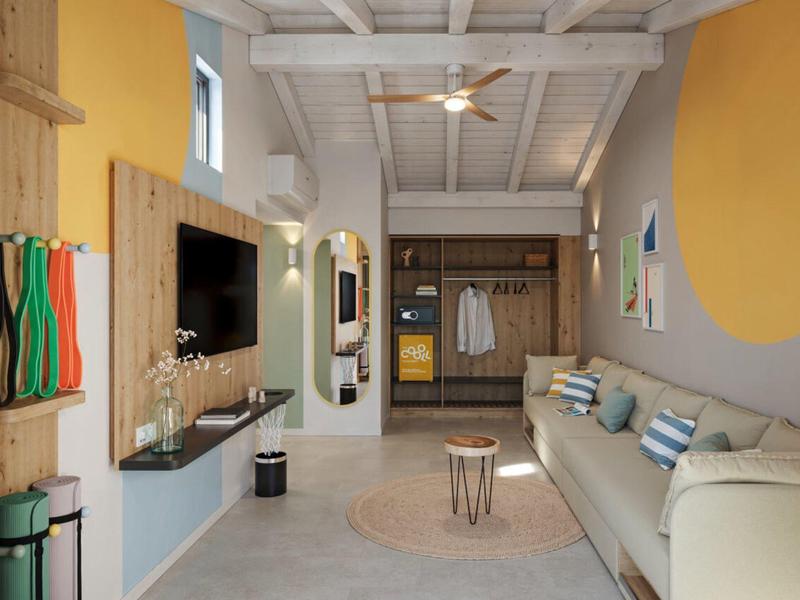 Chambre d'hôtel moderne avec canapé, décoration murale et garde-robe ouverte aux tons clairs.