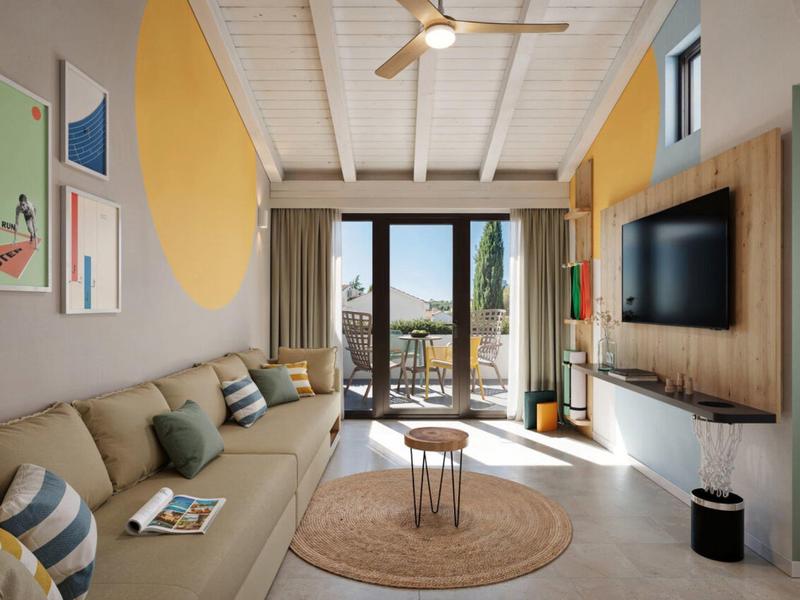 Salon moderne avec canapé clair, grande fenêtre et vue sur terrasse et nature.