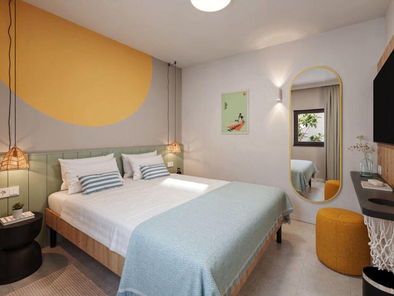 Chambre d'hôtel moderne avec lit double, miroir mural et télévision aux couleurs chaudes.