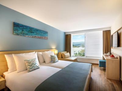 Modern hotel room with two double beds, wooden flooring, and large window with a view.