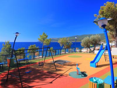 Colorful playground with swings and slide beside blue sea and clear sky.