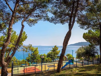 View of a playground by the sea surrounded by trees under clear sky.