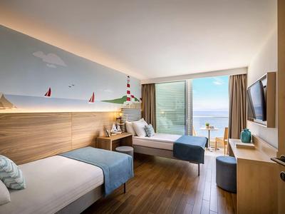 Modern hotel room with two single beds, wooden floor, and sea view through large window.