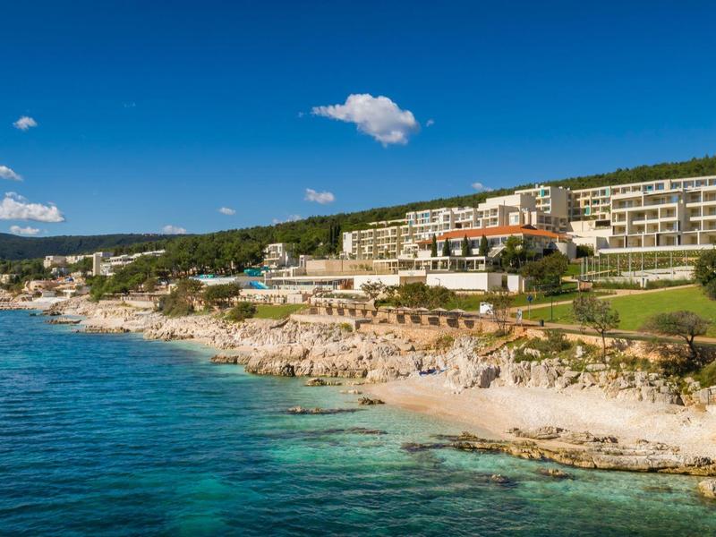 Coastline with clear water, vegetated slope, and large hotels above the beach.