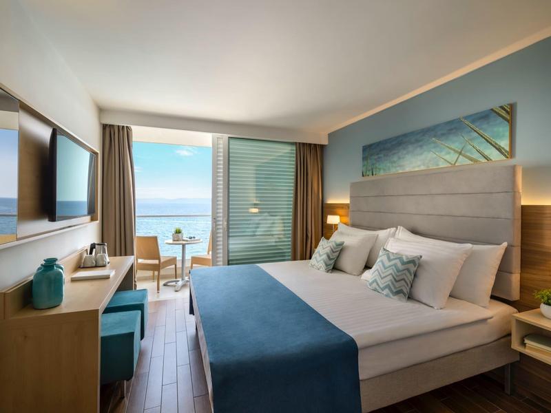 Modern hotel room with sea view, double bed, and balcony.