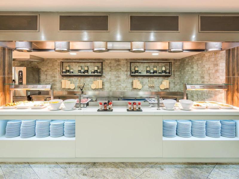 Modern buffet with lighting, white serving stations, and decorative plants in a hotel.