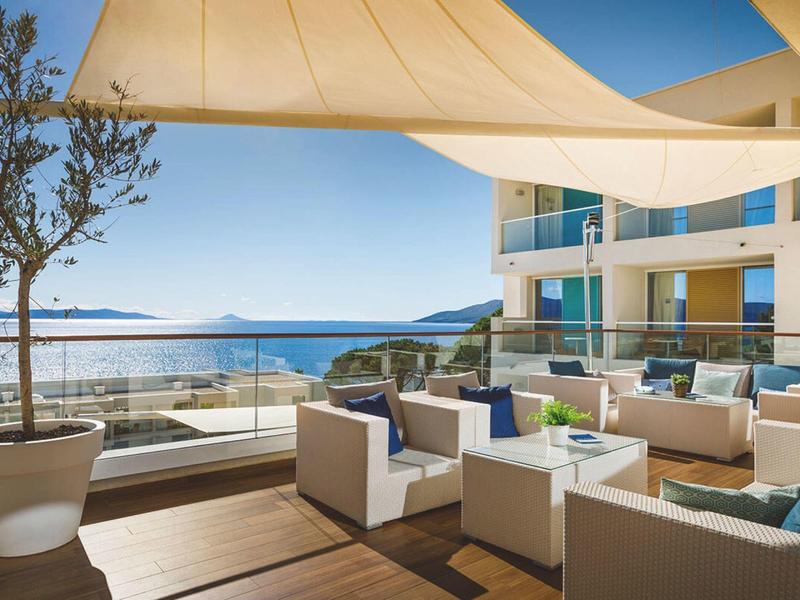 Modern hotel terrace with white lounge furniture, sunshade, and sea view.