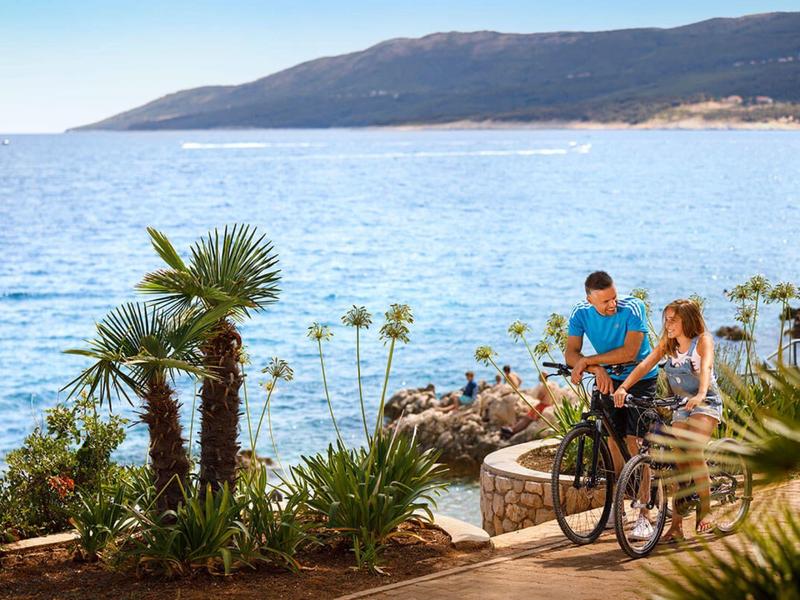 Couple with a bike on a seaside path with hills and palm trees in view