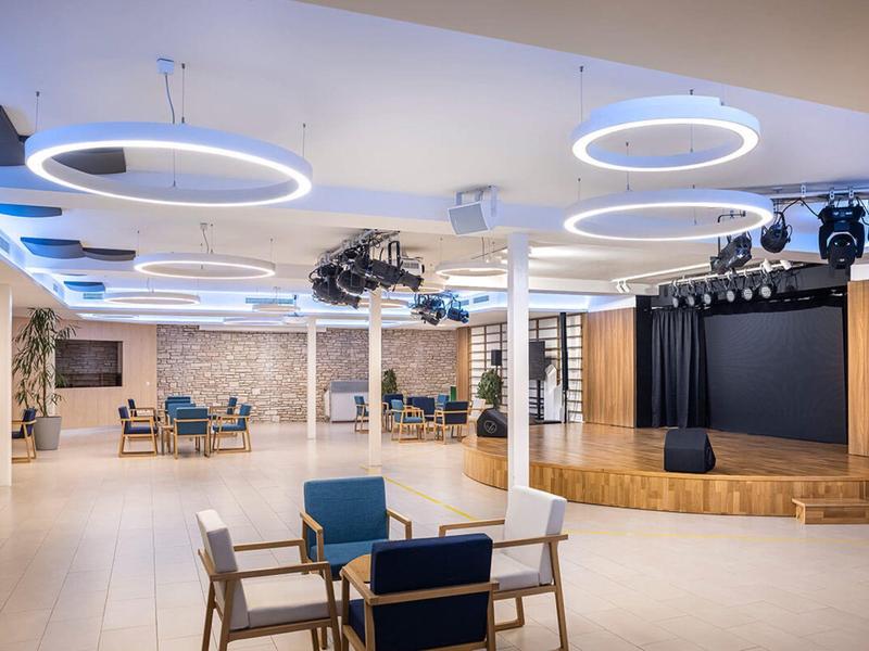 Modern event hall with round stage platform and futuristic ceiling lighting.