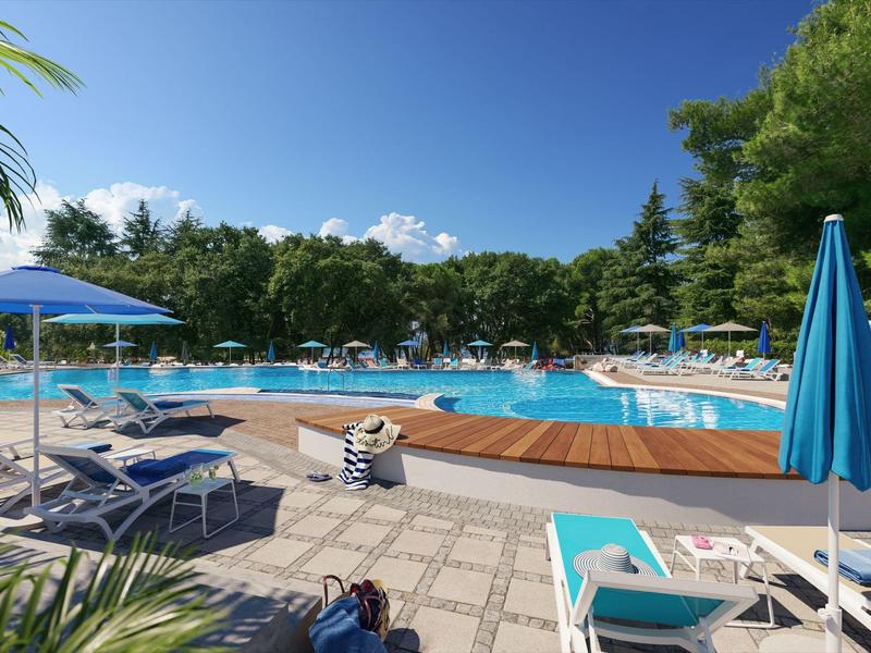 Großer Außenpool mit Liegestühlen, Sonnenschirmen und grünen Bäumen bei klarem Himmel.