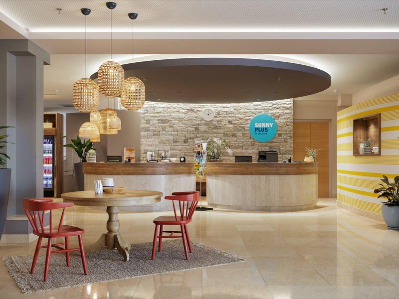 Moderne Hotelrezeption mit rundem Empfangstresen, roten Stühlen und großen Pflanzgefäßen.