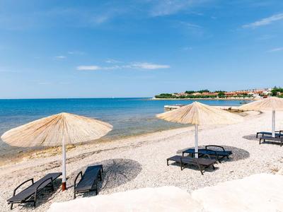 Strand mit weißem Sand, blauen Liegestühlen und Strohmusterschirmen unter blauem Himmel.