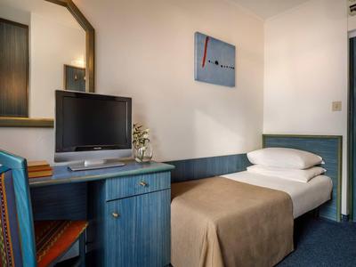 Kleines Zimmer mit Einzelbett, blauem Schreibtisch, Stuhl und kleinem Fernseher an der Wand.