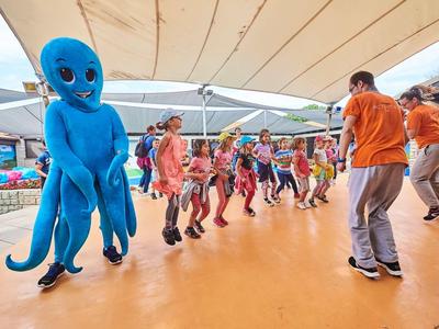 Menschen tanzen auf einer Bühne, eine Person trägt ein großes blaues Oktopus-Kostüm.