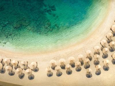 Vista aerea di una spiaggia con acqua blu limpida e file di ombrelloni di paglia.