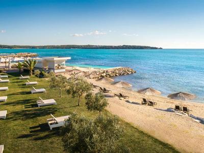 Spiaggia con ombrelloni e lettini accanto a un giardino verde sotto un cielo azzurro