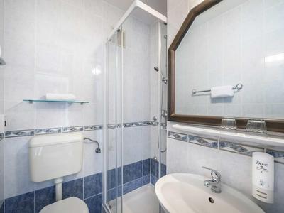 Kleines Bad mit Duschkabine, Toilette, Waschbecken, Spiegel und weißen sowie blauen Fliesen.