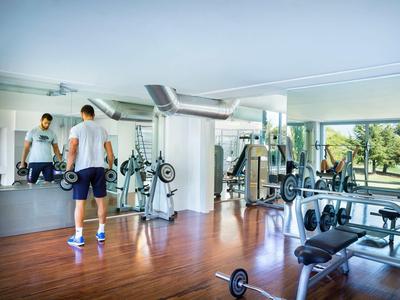 Palestra moderna con parete a specchio, pesi e attrezzi per esercizi accanto a grandi finestre.