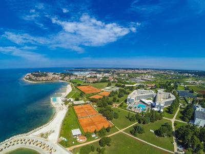 Luftaufnahme einer Küstenstadt mit Stränden, Tennisplätzen, grünen Flächen und Gebäuden unter blauem Himmel.