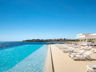 Area piscina lussuosa con lettini e vista sul mare in una giornata soleggiata.