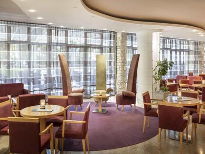 Ristorante dell'hotel luminoso con arredi moderni, moquette e grandi finestre con tende.