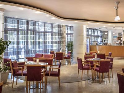 Ristorante luminoso con sedie rosse, tavoli rotondi in legno e un bar sullo sfondo.