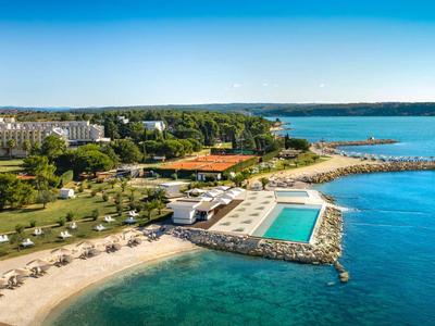 Complesso alberghiero con piscina e spiaggia vicino alla costa sotto un cielo limpido.