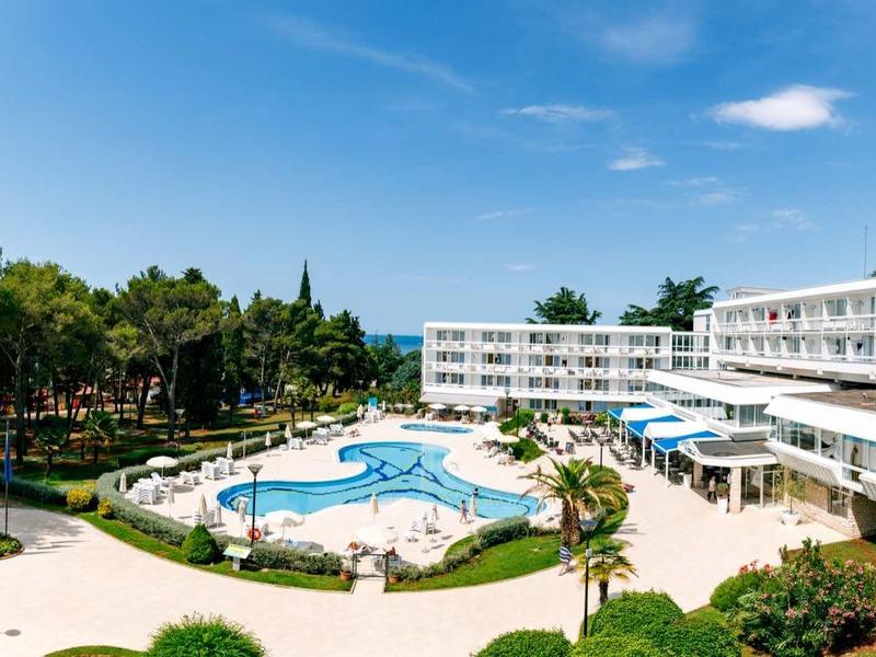 Modernes Hotel mit weißen Gebäuden, Palmen, Pool und blauem Himmel im Hintergrund.