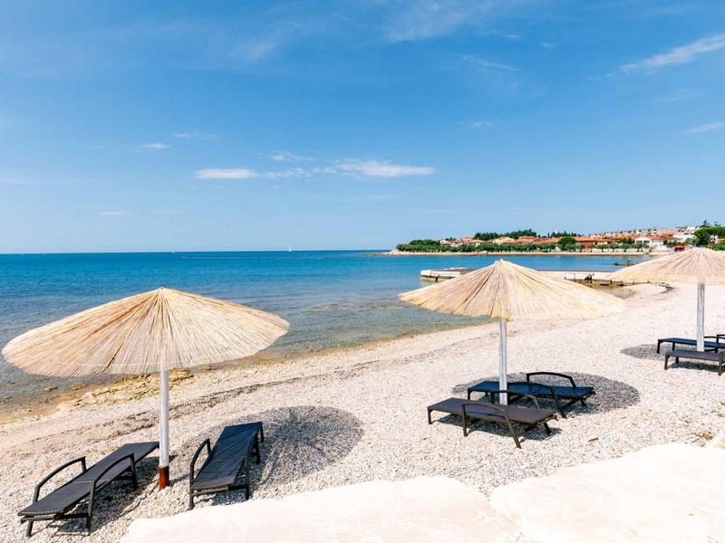 Strand mit weißem Sand, blauen Liegestühlen und Strohmusterschirmen unter blauem Himmel.