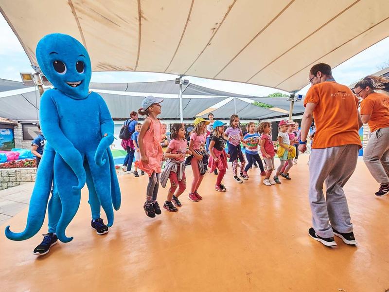 Menschen tanzen auf einer Bühne, eine Person trägt ein großes blaues Oktopus-Kostüm.