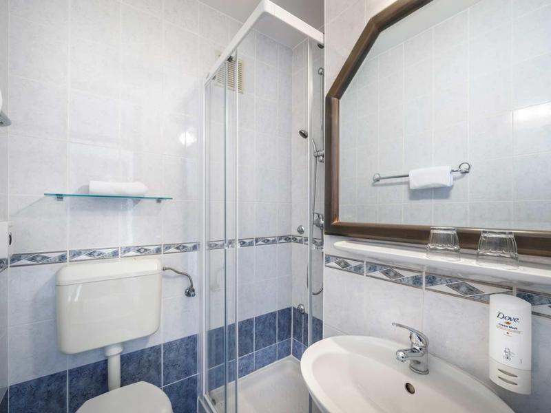 Kleines Bad mit Duschkabine, Toilette, Waschbecken, Spiegel und weißen sowie blauen Fliesen.